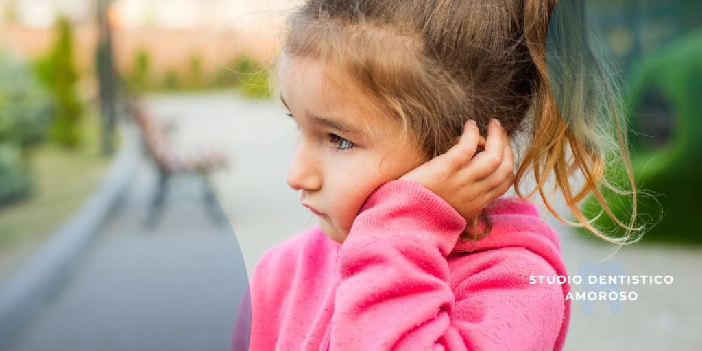 Ipomineralizzazione dei denti: cause, sintomi e trattamenti efficaci Bambina in con espressione di disagio mentre mostra il dolore ai denti, segno tipico della sensibilità causata dalla MIH